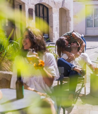 Groupe de personnes sirotant un verre en terrasse ensoleillée, devant un hôtel