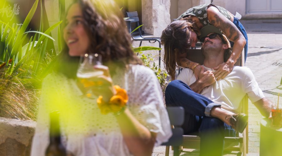 A group of people sipping a drink on a sunny terrace in front of a hotel